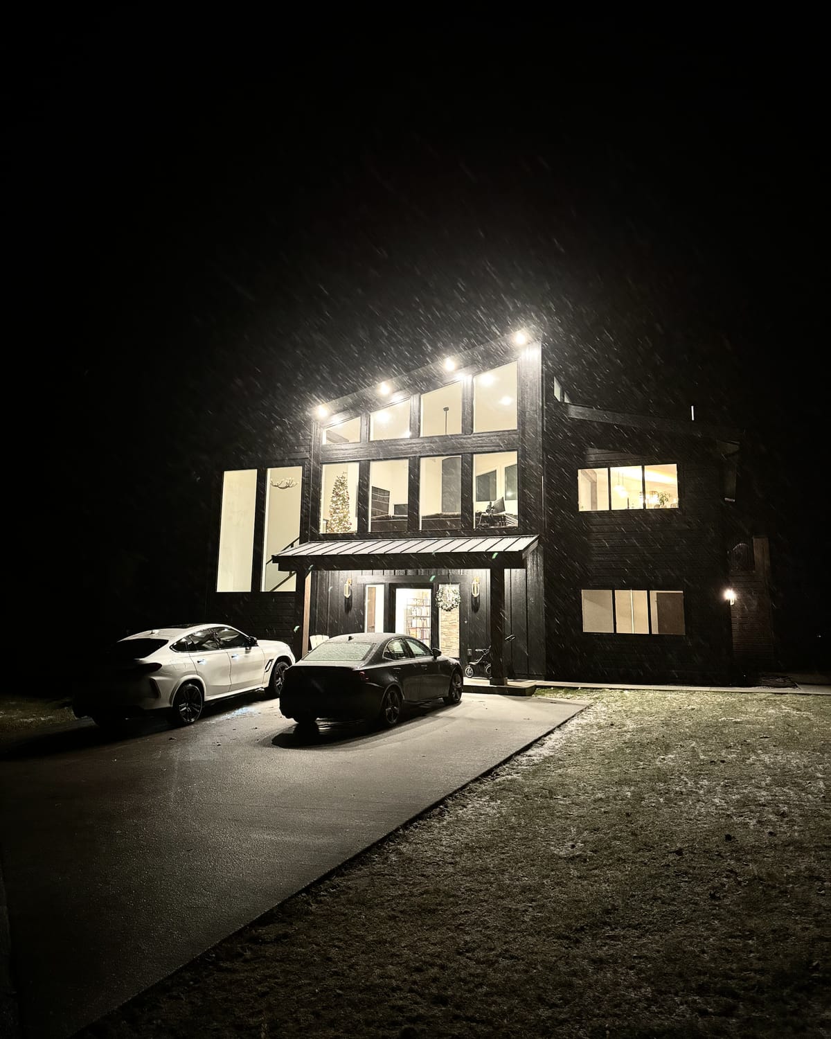 Entry elevation: black lap siding and board-and-batten under an asymmetric shed roofline, with a standing-seam metal canopy on timber posts.