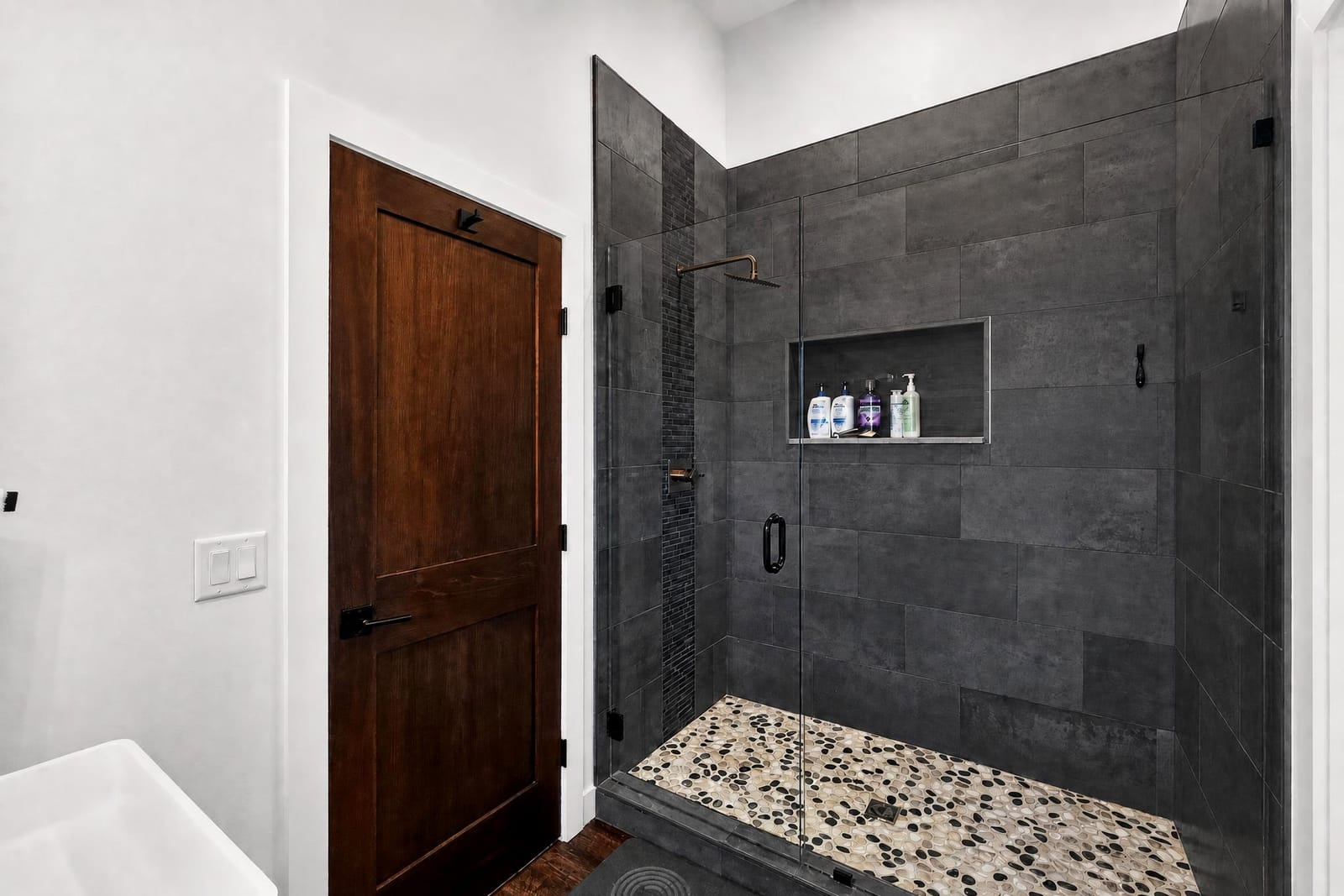 A walk-in shower tiled floor to ceiling in dark stone.